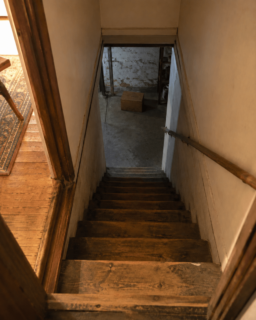 A worn wooden basement staircase leading down toward a single closed box, illustrating how trauma gets stored in the body.