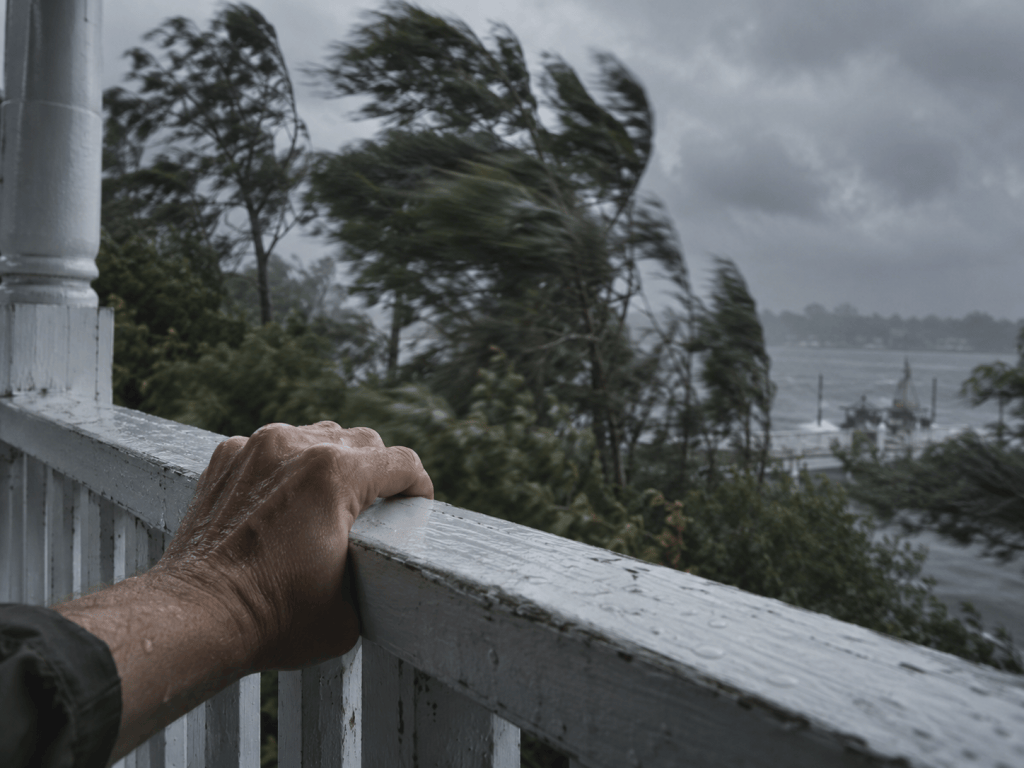 A hand holding onto a porch railing in strong wind